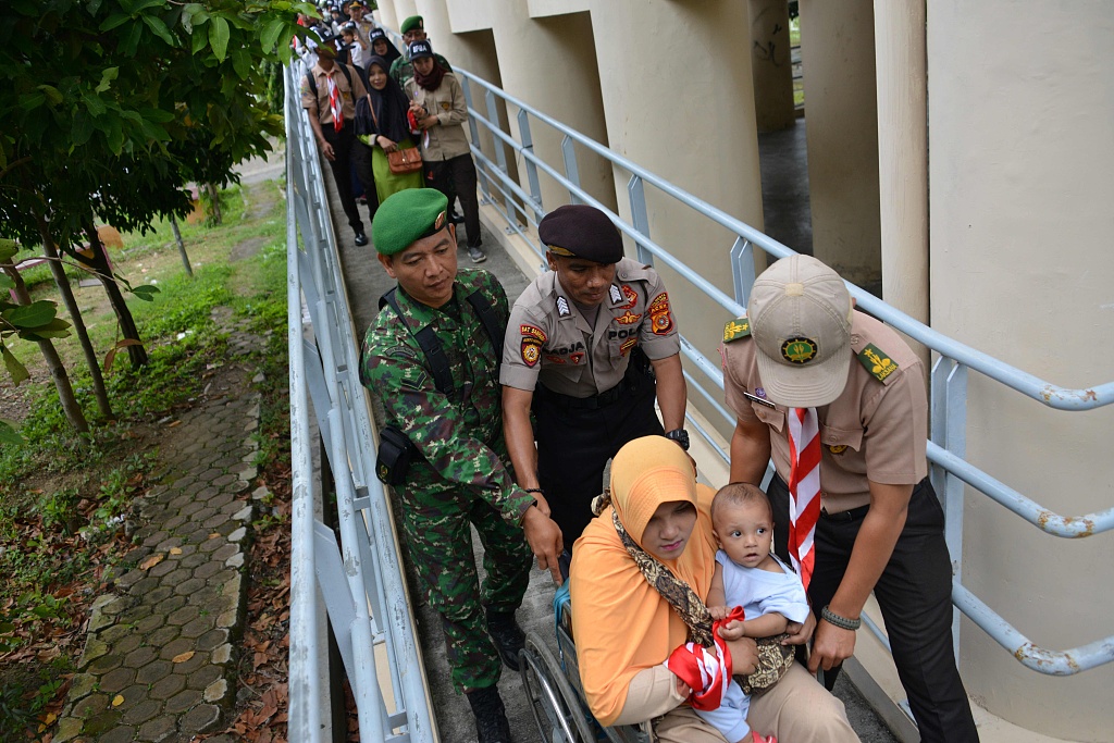 A woman and her baby in a wheelchair are given assistance as they evacuate a building during an earthquake and tsunami drill in Banda Aceh, Indonesia, November 26, 2019. /CFP