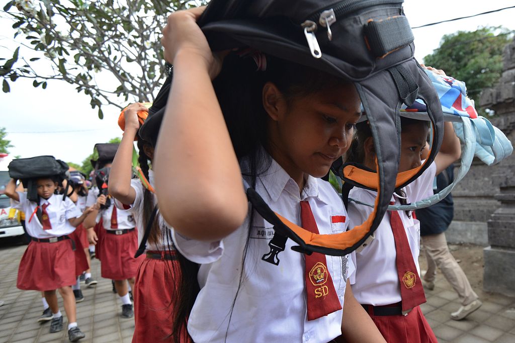 Schoolchildren use their schoolbags to protect themselves during a tsunami drill in Tanjung Benoa near Denpasar on the resort island of Bali, August 15, 2017. /CFP