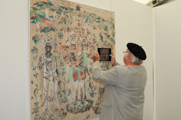 A local visitor attends an exhibition featuring traditional Chinese ink wash paintings on the sidelines of the international cultural and economic exchange event "Blue Container on the New Silk Road" held in Duisberg, North Rhine-Westphalia, Germany. Dunhuang Cave art features various stone carvings and mural paintings. [Photo: China Plus]