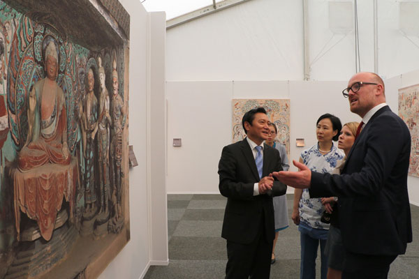 Feng Haiyang (Center), Chinese Consul General in Dusseldorff, and Soren Link (Right), the mayor of Duisberg, visit an exhibition featuring China's Dunhuang Cave art on the sidelines of the international cultural and economic exchange event "Blue Container on the New Silk Road" held in Duisberg, North Rhine-Westphalia, Germany. Dunhuang Cave art features various stone carvings and mural paintings. [Photo: China Plus]