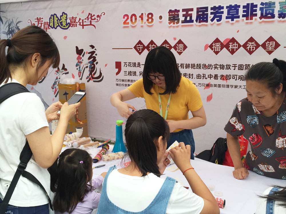 A few visitors to the annual cultural heritage festival in Beijing try to make kaleidoscopes during China's Cultural Heritage Day on Saturday, June 9, 2018. [Photo: China Plus]
