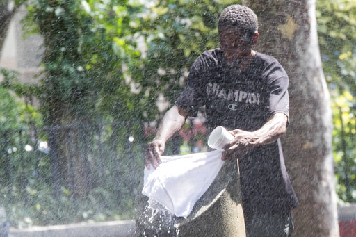 A man uses a park sprinkler to cool off, Wednesday, Aug. 29, 2018, in New York. Dangerously high heat in the Northeastern United States has prompted emergency measures including extra breaks for players wilting at the U.S. Open tennis tournament. [Photo: AP/Mary Altaffer]