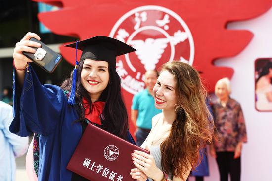 A foreign student takes a selfie at her graduation ceremony at Zhejiang University on June 28, 2018. (Photo/Xinhua)