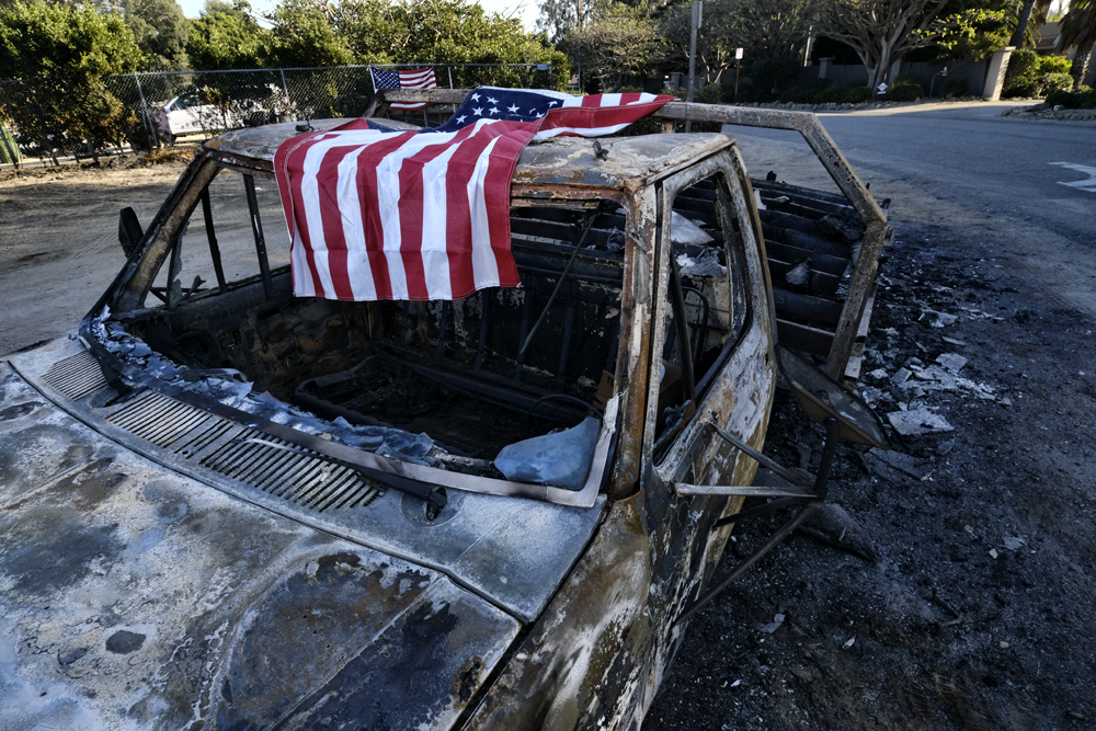 An American flag is draped over the charred remains of an old pickup truck entering Point Dume along the pacific coast highway in Malibu, Calif., on Sunday Nov. 11, 2018. [Photo: AP/Richard Vogel]