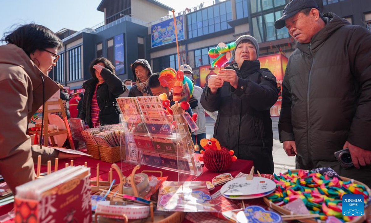 People select Fanlihua, a paper-made traditional flipping toy, at a stall during a festive fair held at the Longfusi commercial area in Dongcheng District of Beijing, capital of China, Feb. 12, 2026. The fair held in celebration of the upcoming Spring Festival creates diverse consumption scenarios for citizens and tourists. It will last until March 3. (Xinhua/Ju Huanzong)

