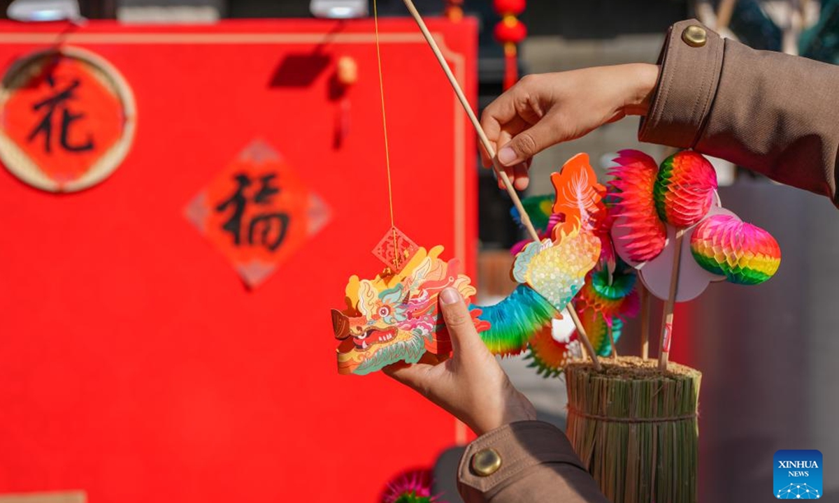 A staff member arranges Fanlihua, a paper-made traditional flipping toy, during a festive fair held at the Longfusi commercial area in Dongcheng District of Beijing, capital of China, Feb. 12, 2026. The fair held in celebration of the upcoming Spring Festival creates diverse consumption scenarios for citizens and tourists. It will last until March 3. (Xinhua/Ju Huanzong)

