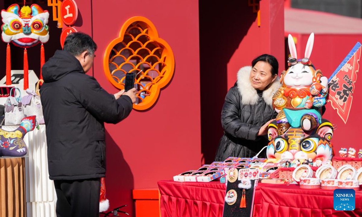 A tourist poses for photos with a Lord Rabbit, known as Tu'er Ye in Chinese (a traditional handicraft and a festive clay toy for children, especially in Beijing), during a festive fair held at the Longfusi commercial area in Dongcheng District of Beijing, capital of China, Feb. 12, 2026. The fair held in celebration of the upcoming Spring Festival creates diverse consumption scenarios for citizens and tourists. It will last until March 3. (Xinhua/Ju Huanzong)