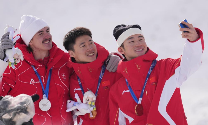 Gold medalist Wang Xindi (C) of China, silver medalist Noe Roth (L) of Switzerland, and bronze medalist Li Tianma of China take a selfie during the awarding ceremony of the freestyle skiing men's aerials at the Milan-Cortina 2026 Olympic Winter Games in Livigno, Italy, Feb. 20, 2026. (Xinhua/Hu Chao)