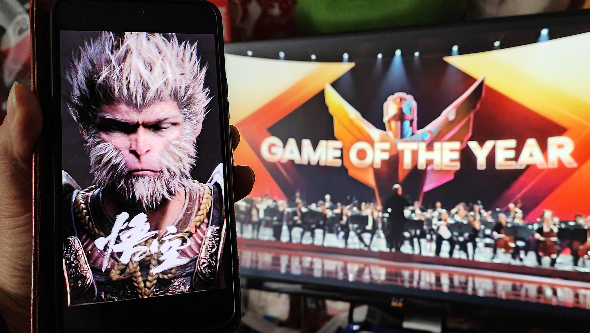 A gamer in Shanghai holds up a phone displaying a Black Myth: Wukong poster while watching the game win the Game of the Year Award at The Game Awards (TGA) 2024 ceremony in December 2024. /VCG