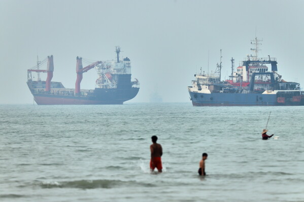 Children wade in the water with cargo ships at anchor in the background and a fisherman nearby, in the Strait of Hormuz off Bandar Abbas, Iran, Tuesday, June 30, 2026. (Amirhosein Khorgooi/ISNA via AP,File)